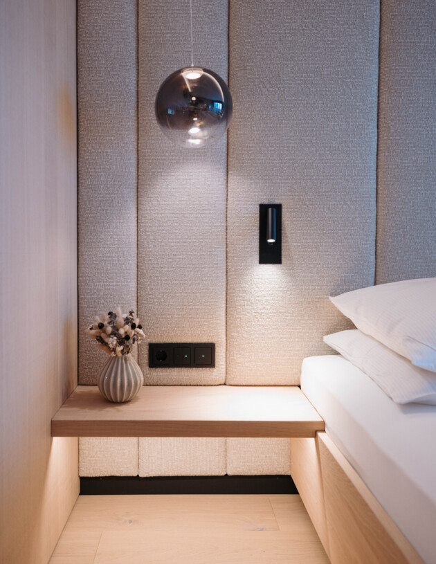 Detailaufnahme Zimmer mit Nachtkasten und Lampe.