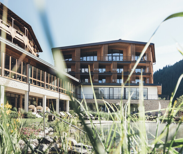 Wellnesshotel Nesslerhof in Großarl mit Naturbadeteich und Garten im Sommer.